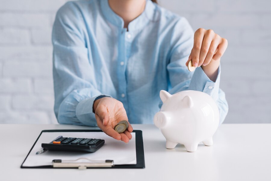 businesswoman-showing-coins-with-white-piggybank-desk_23-2147892149